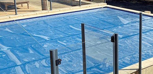 A Blue Pool Cover and Glass Fencing in Pool Area — Pool Cover Systems in Melbourne, VIC